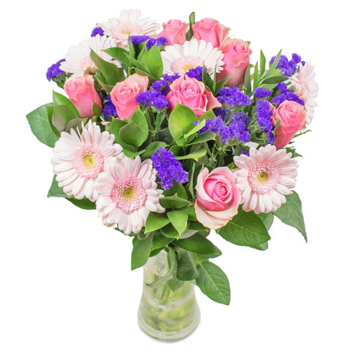 A lavish, thoughtfully composed bouquet displayed in a clear glass vase, backed by pristine white, as if freshly arranged in a Carshalton florist's sunlit window. This eye-catching centrepiece showcases around seven to nine pink roses-some with tightly swirled buds, others just beginning to open, revealing classic spiral shapes and velvety, blushing petals. Complementing them are five to seven light pink gerbera daisies, their broad, round faces and nearly white centres adding a youthful warmth. Between these, vivid purple statice flowers are woven in, adding depth, texture, and a pop of colour that enlivens the composition, their forms echoing the vibrancy of local wildflower patches. The bouquet's abundant base of rich, deep green foliage grounds the display with freshness and volume, the stems visible through the water in the vase, underscoring its just-gathered authenticity. This arrangement suggests the joy of celebrations in Carshalton-perfect for birthdays, anniversaries or as a gracious gesture for Mother's Day-each bloom thoughtfully chosen to express warmth, cheer, and the welcoming spirit of the SM5 community.